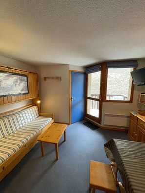 A compact room with a striped sofa, a small wooden table, a bed, a television, and a window with a view. - 200 meters from the ski slopes, 1st floor, balcony, TV, 23 m², Peisey-Vallandry (Peisey-Nancroix)