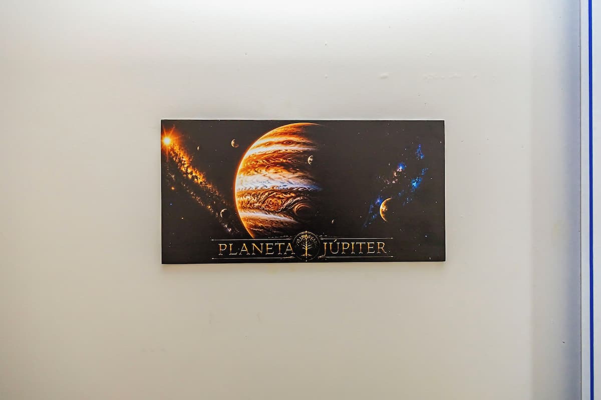 Póster colgado en la pared de Júpiter, con el texto 'PLANETA JUPITER' y una representación de las lunas del planeta.