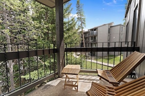 Ein Balkon mit Holztisch und zwei Lounge-Sesseln mit Blick auf einen Garten und Gebäude.