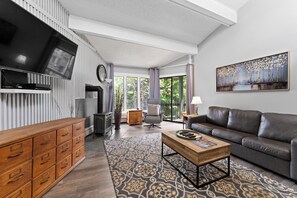 Ein modernes Wohnzimmer mit Flachbildfernseher, Sofa, Couchtisch und einem gemusterten Teppich.