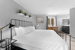 Ein Schlafzimmer mit einem Bett, Nachttischen, einem Schreibtisch, einer Kommode, einem Spiegel und einem Fenster mit Vorhängen.