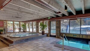 Ein großer, überdachter Swimmingpool mit einer Holzterrasse und einem separaten Whirlpoolbereich.