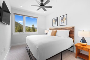 A bedroom with a bed, a ceiling fan, a TV, a window with a mountain view, and two framed pictures on the wall. - Steps from Lakeside Village w/ Lodge & Spa Access (Keystone)