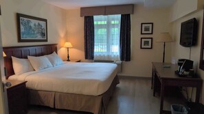 Ein Hotelzimmer mit Bett, Nachttisch, Lampe, Schreibtisch, Stuhl und Fernseher.