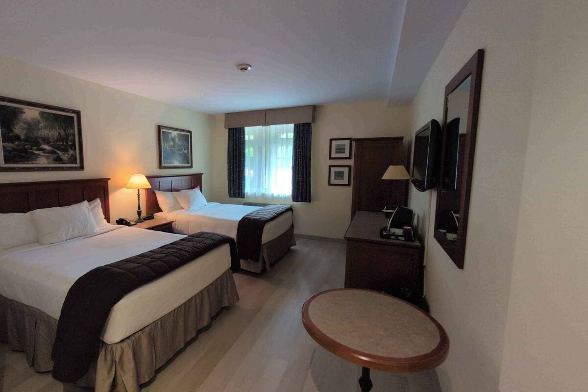 A hotel room with two beds, a desk, a chair, a round table, and a TV.