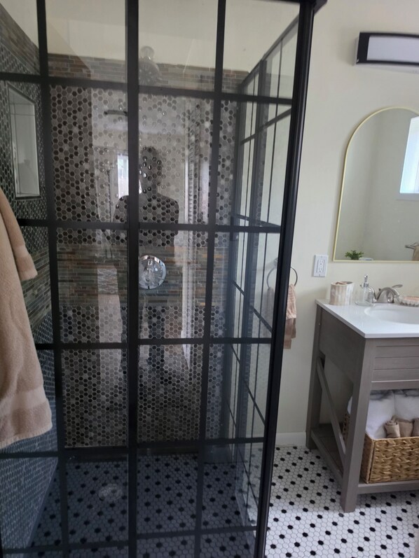 Ein Badezimmer mit Glasdusche, Waschbecken mit Toilettenartikeln und Spiegel.