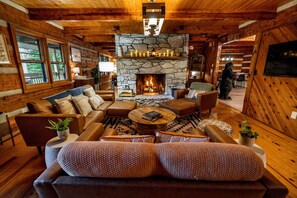 A cozy cabin interior with a stone fireplace, leather furniture, and wooden walls. - Log Cabin, Theater, Arcade & Sauna | Beaver Cabin (Weaverville)