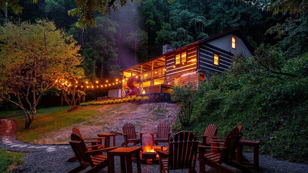 Eine Hütte mit Terrasse, umgeben von Bäumen und einer Feuerstelle mit Sitzgelegenheiten.