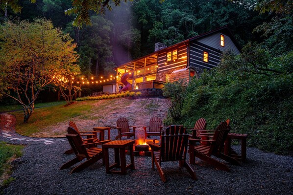 A cabin with a deck, surrounded by trees and a fire pit with chairs. - Log Cabin, Theater, Arcade & Sauna | Beaver Cabin (Weaverville)