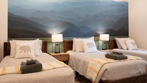 Une chambre d’hôtel avec deux lits, chacun agrémenté d’une fresque murale représentant un paysage de montagne, d’une tête de lit en bois et d’une table de chevet avec une lampe.