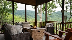 Un espace extérieur aménagé, abrité et doté de mobilier en osier, d’un foyer et d’une vue sur une chaîne de montagnes boisée.