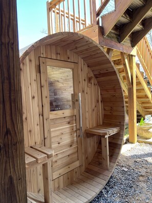 Eine Holzsauna mit Tür, einer kleinen Sitzbank und einer Steinwand.