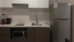 Una cocina con armarios blancos, un refrigerador de acero inoxidable, una cafetera y un microondas.