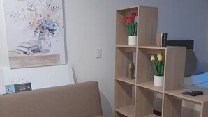 Una sala de estar con un sofá color beige, una estantería de madera y un cuadro en la pared.
