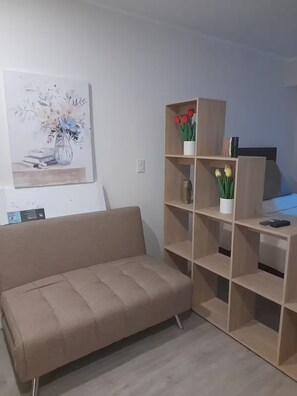 A living room with a beige sofa, a wooden bookshelf, and a painting on the wall. - Cozy 1-bedroom studio in gorgeous Miraflores with AC (Miraflores)