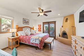 Ein Schlafzimmer mit Bett, Nachttischen, Deckenventilator, Kamin und Fernseher.
