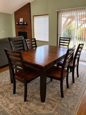 A dining area with a wooden table and chairs, a fireplace, and a large window with blinds. - Modern 3BR Home Near UO, Autzen Stadium, Oakway Center & Hayward Field (Eugene)