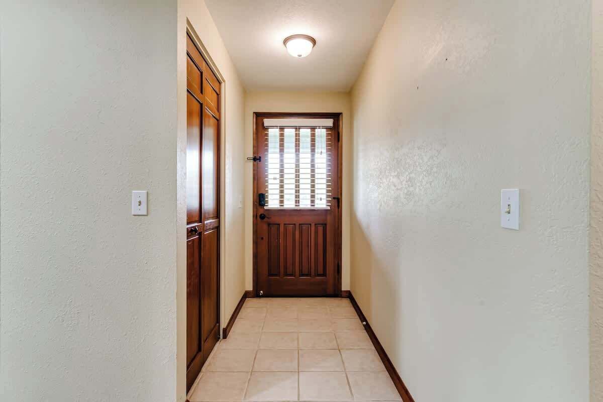 Un couloir étroit avec une porte en bois, un interrupteur et un luminaire au plafond.