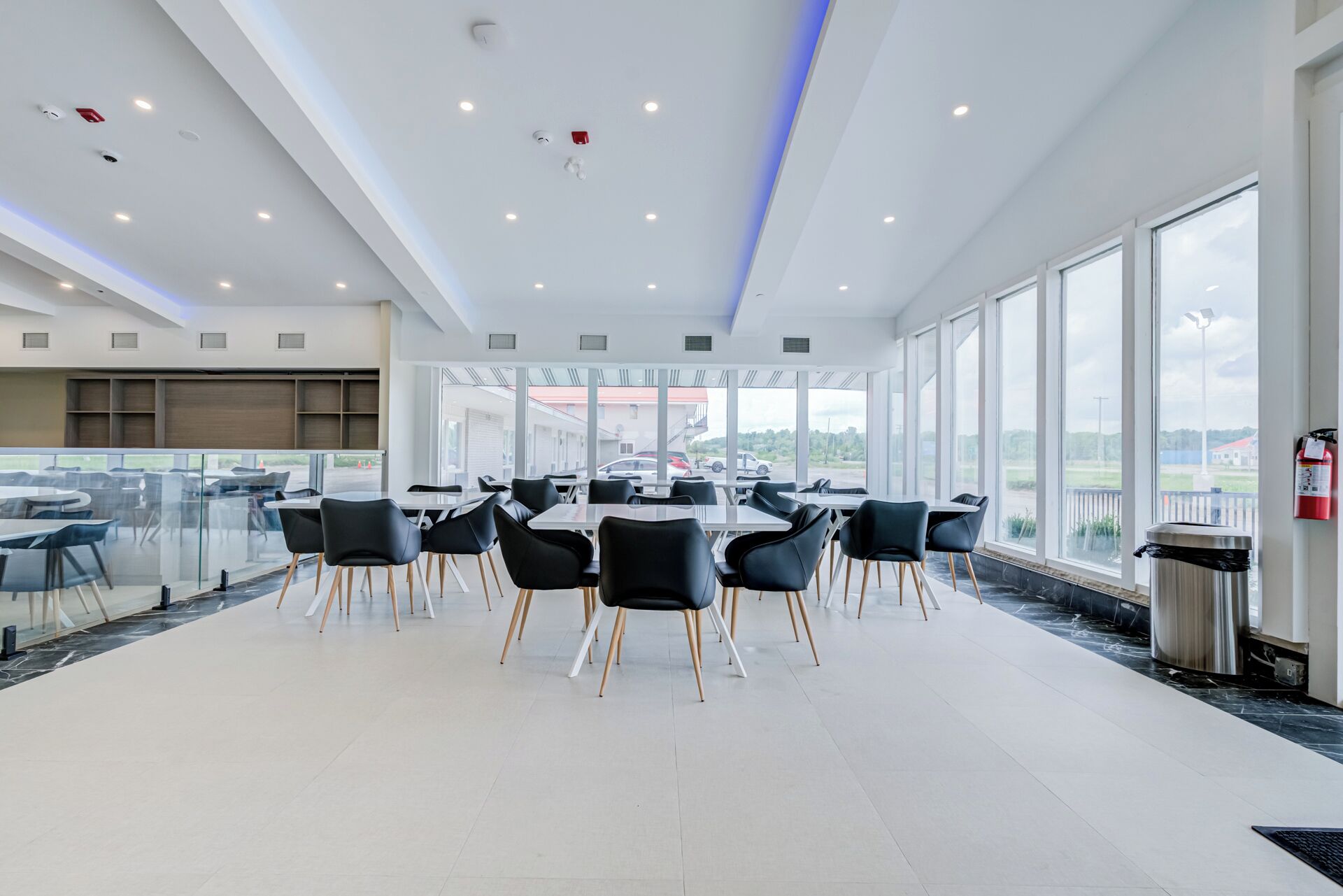 A spacious indoor area with tables and chairs, large windows, and a view of the outside.