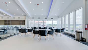 A spacious indoor area with tables and chairs, large windows, and a view of the outside.