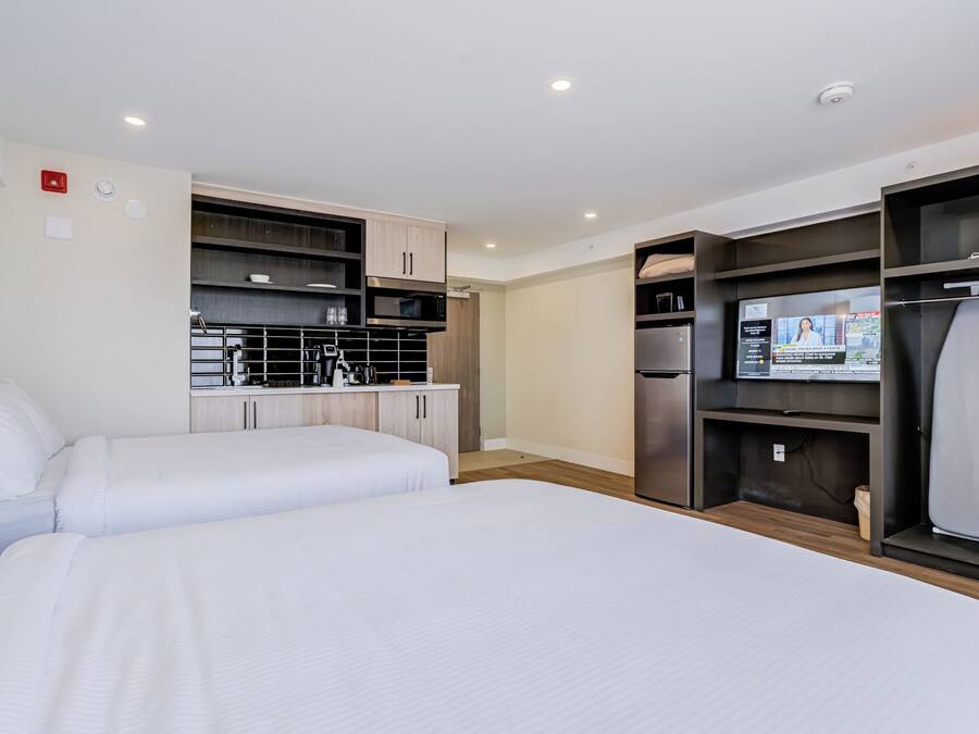 Habitación de hotel con dos camas, kitchenette, televisor de pantalla plana y armario.