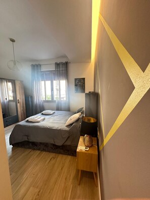 Une chambre à coucher avec un lit, une table de chevet, une lampe et une fenêtre avec des rideaux.