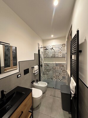 Une salle de bain moderne avec un lavabo noir, des toilettes blanches et un espace douche agrémenté de carreaux à motifs.