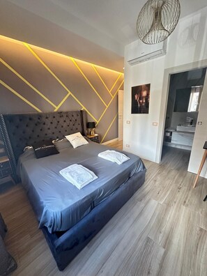 Une chambre à coucher moderne, dotée d’un grand lit, d’une table de chevet, d’une lampe et d’un climatiseur fixé au mur.