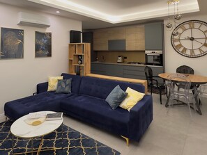 Un salon moderne avec un canapé bleu, une petite table ronde et une cuisine en arrière-plan.