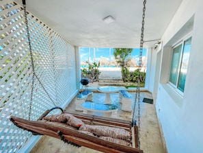 A room with a swing, a small table, a chair, and a view of the beach. - Caribbean Los Corales Villas Suite SPA (Punta Cana)