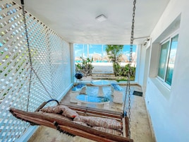 Una habitación con una hamaca, una mesita, una silla y vista a la playa.