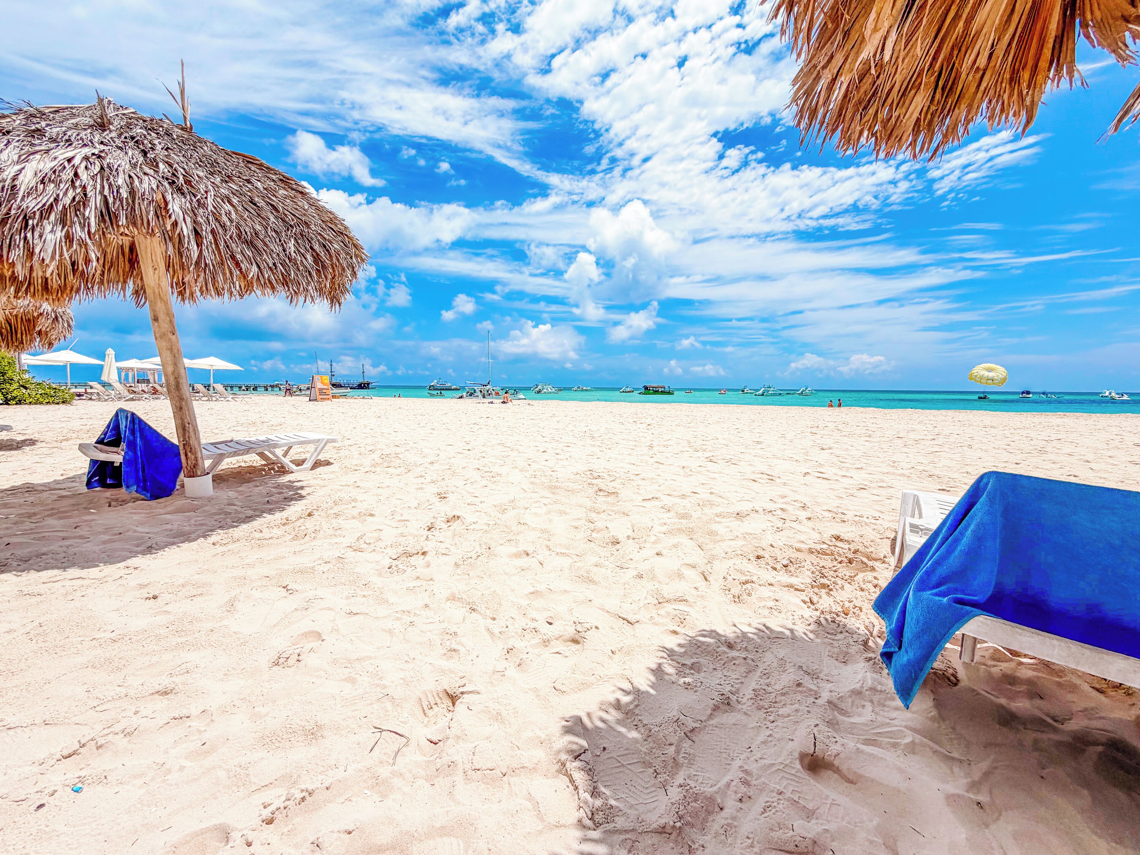A beach with lounge chairs, a thatched umbrella, and a clear view of the ocean.