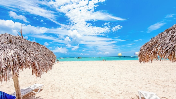 Een strand met rieten parasols, een helderblauwe lucht en een rustige zee.