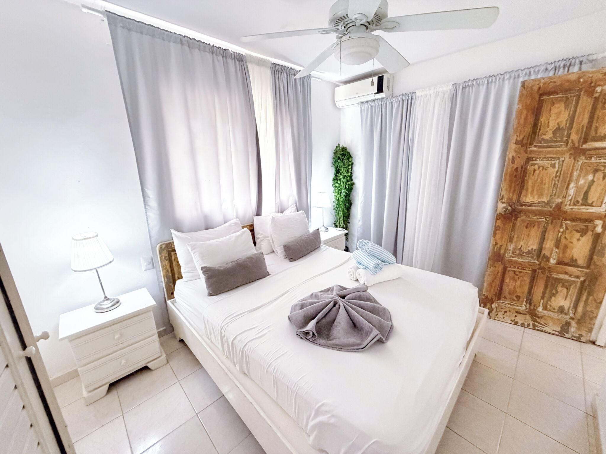 A bedroom with a bed, a nightstand, a lamp, a ceiling fan, and a wooden door.