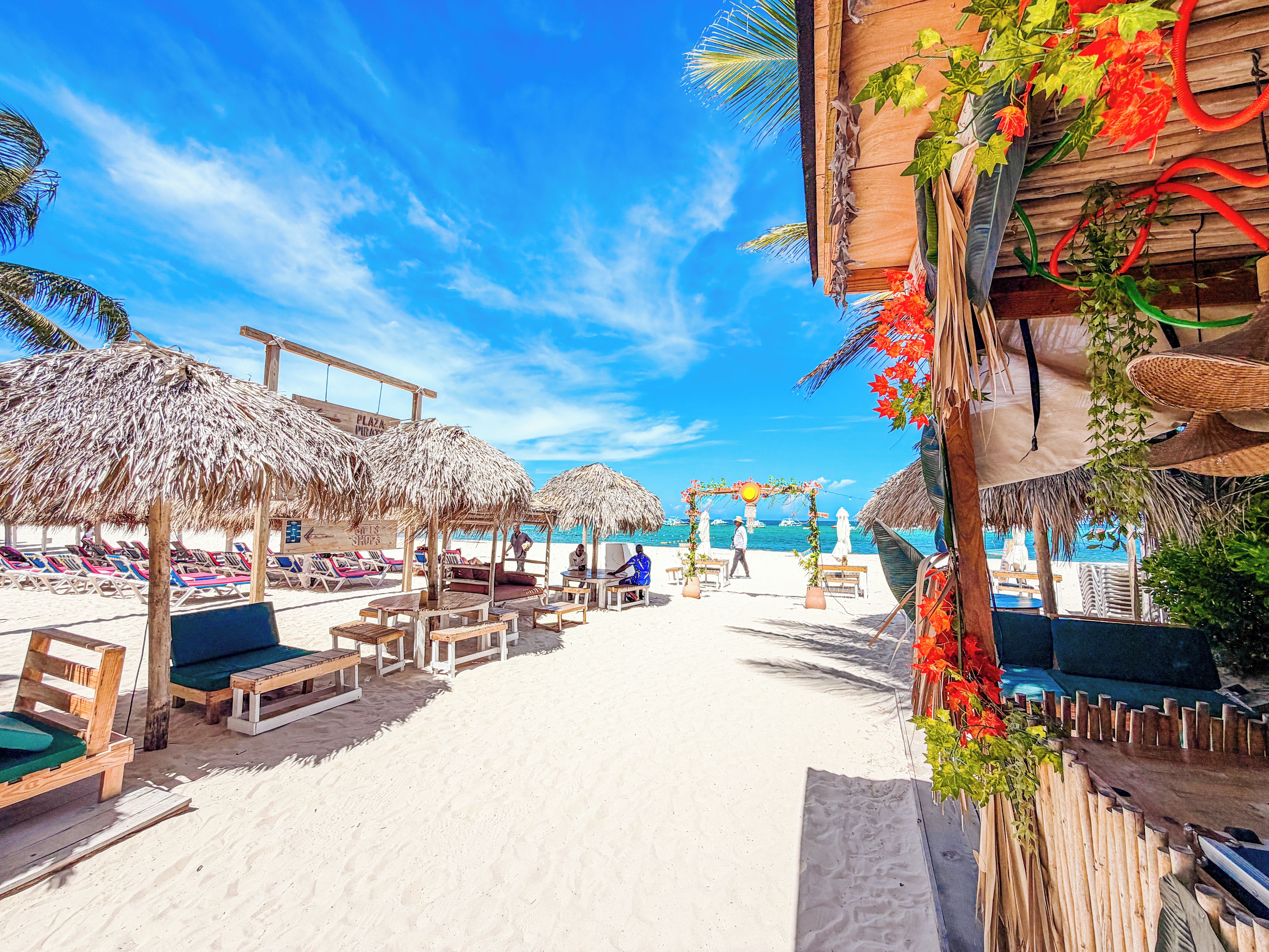 A beach setting with thatched umbrellas, wooden lounge chairs, and a sandy beach.