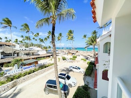 A beach view with palm trees, a beach club sign, and parked cars.