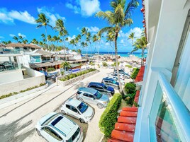 A beachside view with parked cars, a beach club, and palm trees.