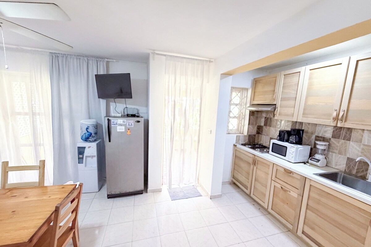 A kitchen with a refrigerator, microwave, and stove. There is a dining table with chairs.