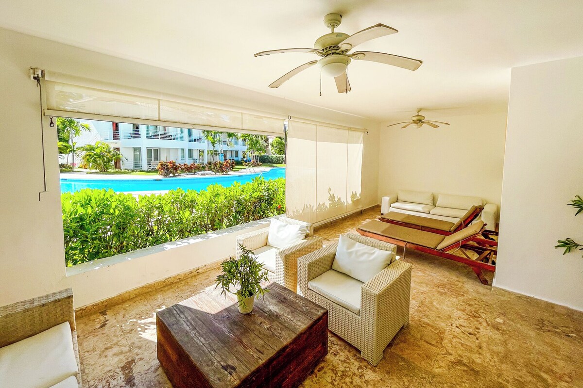 A room with a view of a swimming pool, a ceiling fan, a sofa, and a coffee table.