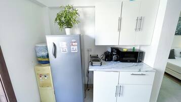 Petita cuina compacta amb nevera, microones, cafetera i dispensador d'aigua.