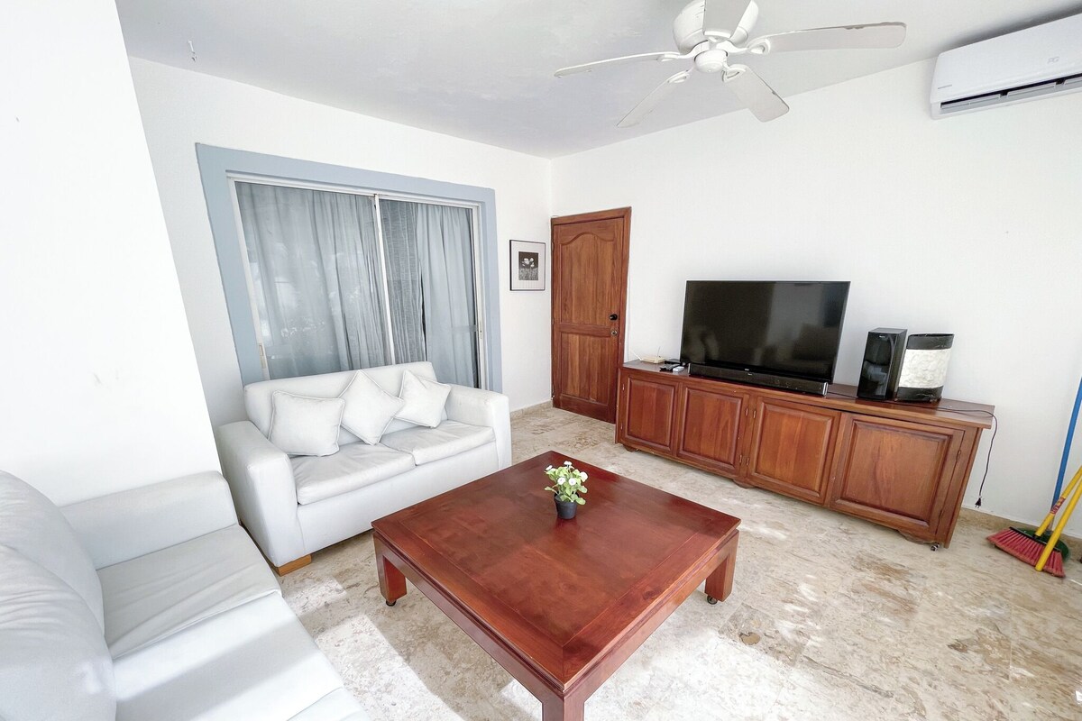 A living room with a white sofa, a wooden coffee table, a television on a wooden cabinet, and a ceiling fan.