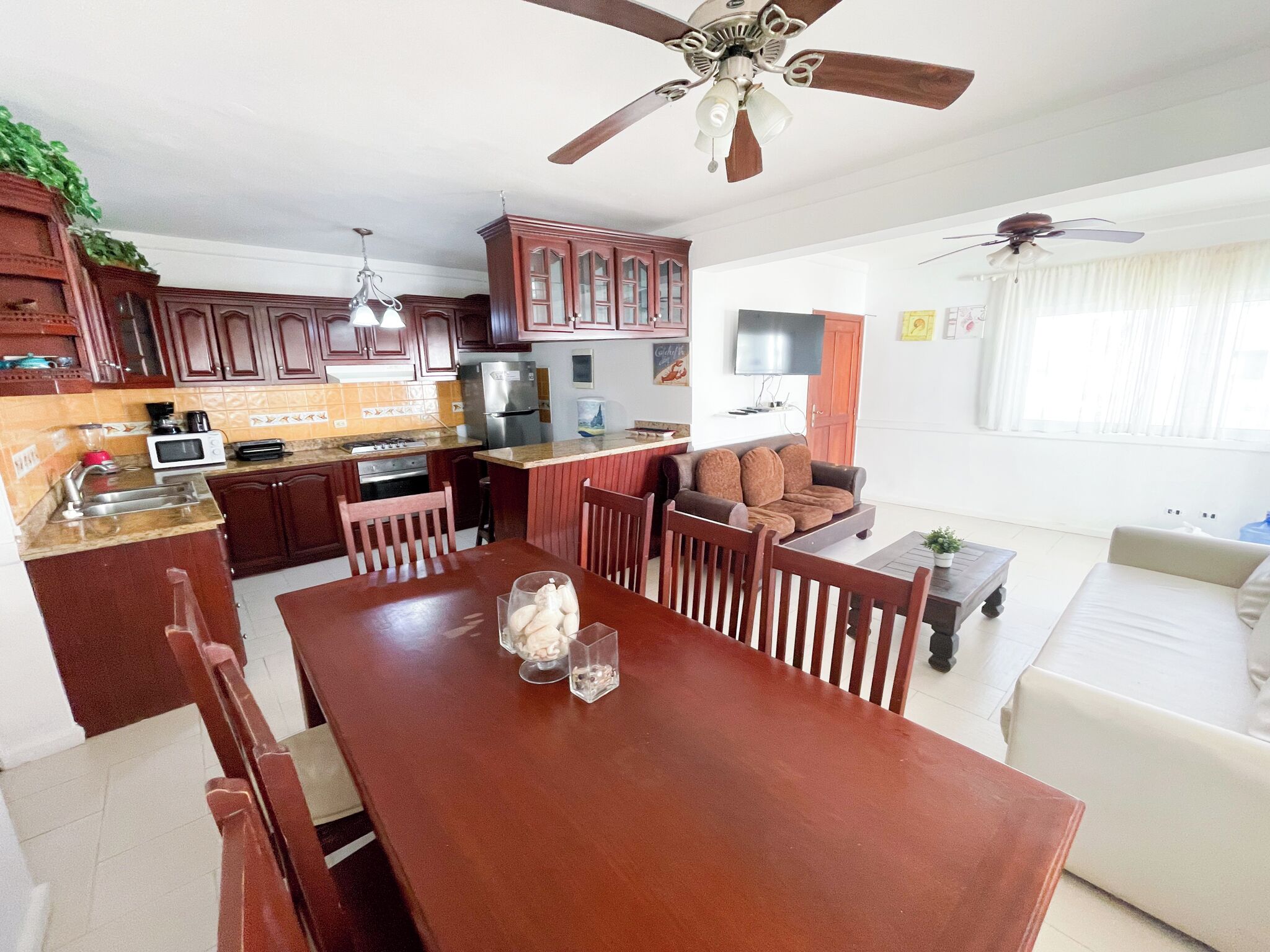 A modern kitchen with a dining area, wooden cabinets, a built-in oven, and a ceiling fan.