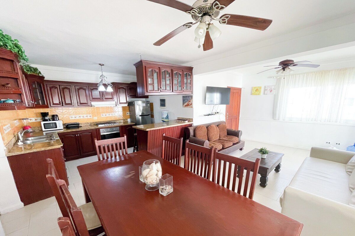 A modern kitchen with a dining area, wooden cabinets, a built-in oven, and a ceiling fan.