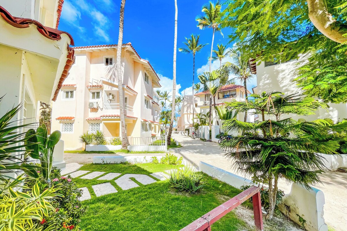 Una strada residenziale con case, palme e un cielo azzurro limpido.