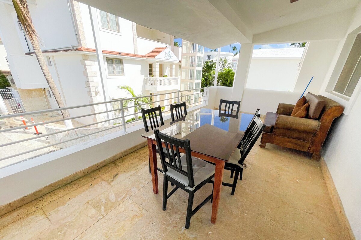 Zona pranzo con tavolo e sedie in vetro, un balcone con ringhiera e vista sugli edifici vicini.