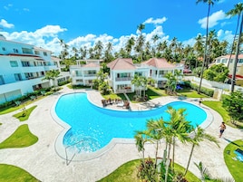 A resort with a large swimming pool, multiple buildings, and palm trees.