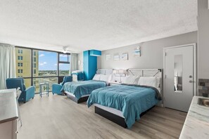 Quarto de hotel com uma grande janela, duas camas, uma escrivaninha e uma cadeira.