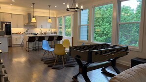 Una cocina moderna con mesa de futbolín, taburetes de bar y ventanas amplias.