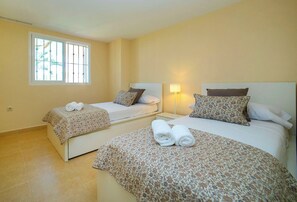 A hotel room with two beds, a window, and a nightstand with a lamp.