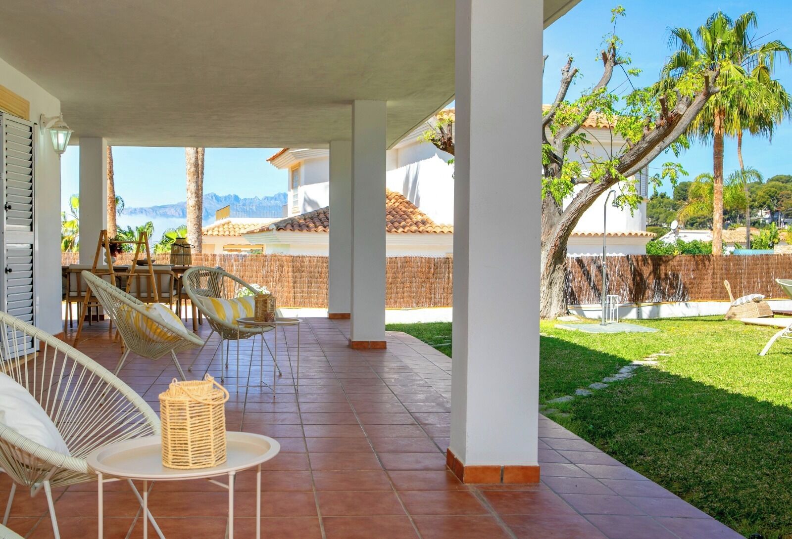 A covered patio with wicker furniture, a view of mountains, and a well-maintained lawn.